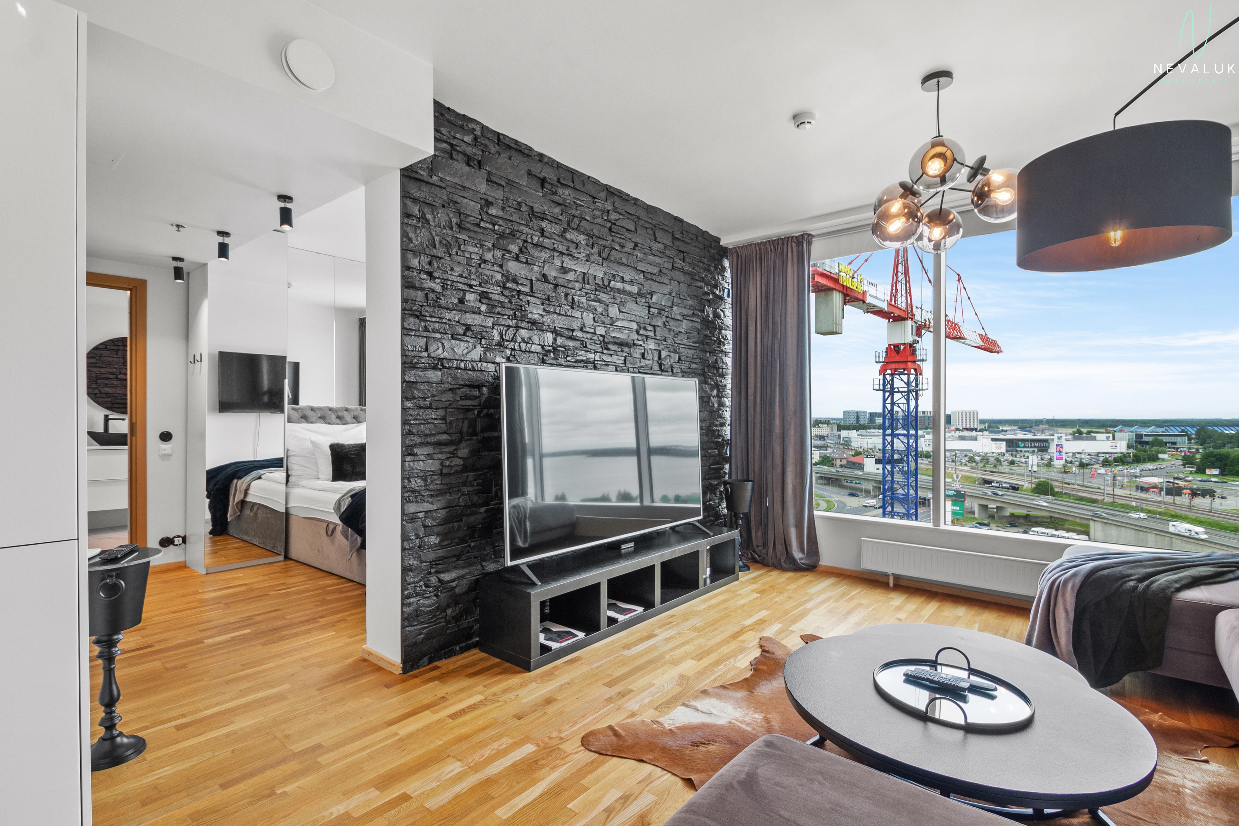 Avatud planeeringuga elutuba Fahle majas musta dekoratiivkiviseina, teleri ja suure aknaga, millest avaneb vaade Tallinnale