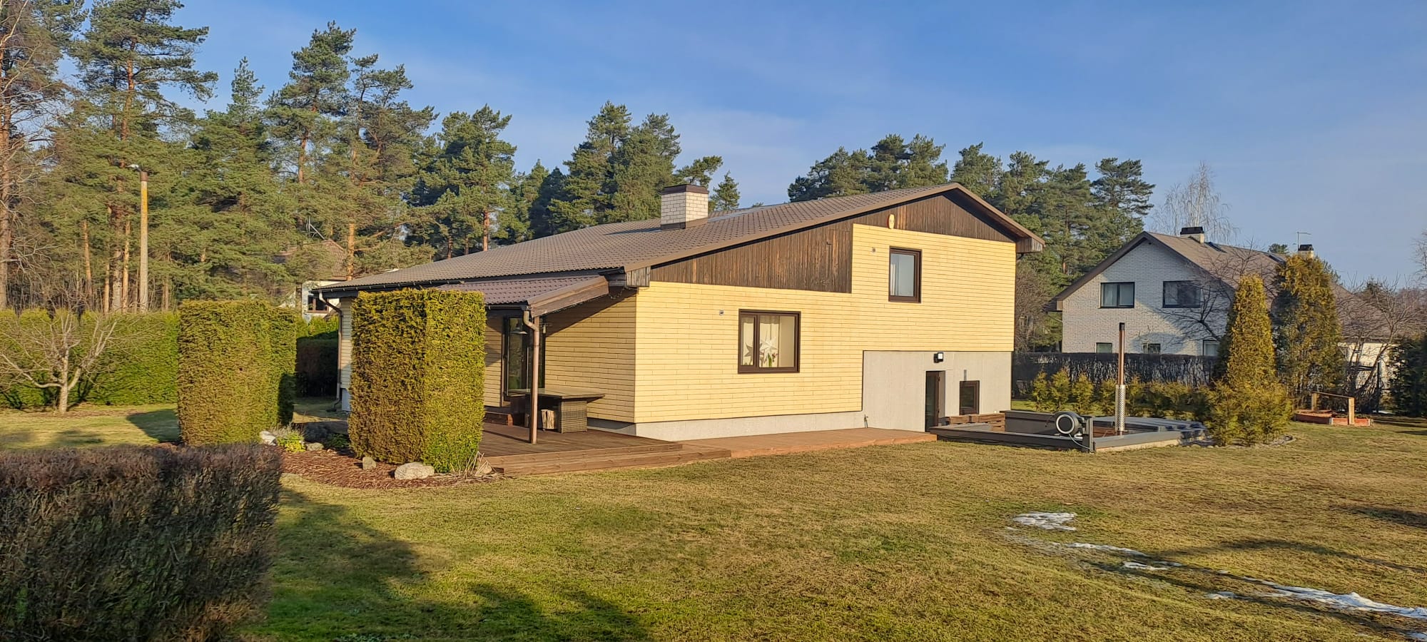 Kollane voodrilaud fassaadil, suur muruplats ja kõrged männid taustal Põllu tn 20 kinnistul